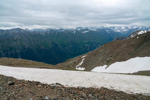 A drone flies over a mountain valley in the Caucasus Mountains. The valley is filled with green trees and a winding river. In the distance, a snow-capped peak rises above the valley.