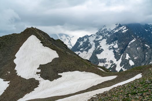 A drone flies over a mountain valley in the Caucasus Mountains. The valley is filled with green trees and a winding river. In the distance, a snow-capped peak rises above the valley.