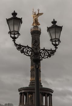 Berlin, Germany - Dec 20, 2023 - Street lamppost with The victory column in the background. Upper part of the Victory column with Goddess Victoria to Celebrate Prussia's victory in the Franco-German War in the Tiergarten. Copy space, Selective focus.