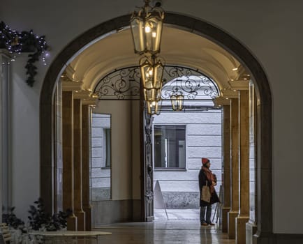 Munich, Germany - Dec 21, 2023 - Side view A woman standing and looking at showcase the products on display in building with Beautiful antique lantern hanging from ceiling. Space for text, Selective focus.