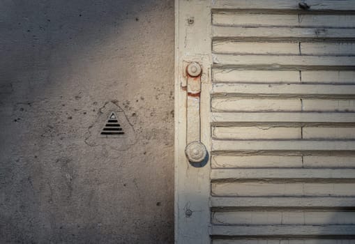 France, Paris - Jan 03, 2024 - The sun is shining through Vintage French Louvred Shutters and Knapen Siphons on wall (to vent damp air from inside the wall). Space for text, Selective focus.