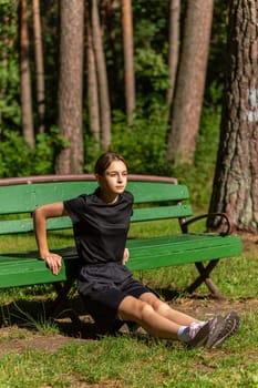 Beautiful young sporty woman in black t-shirt, black shorts and pink trainers warming up exercising triceps dip doing push-ups from bench among trees before running.