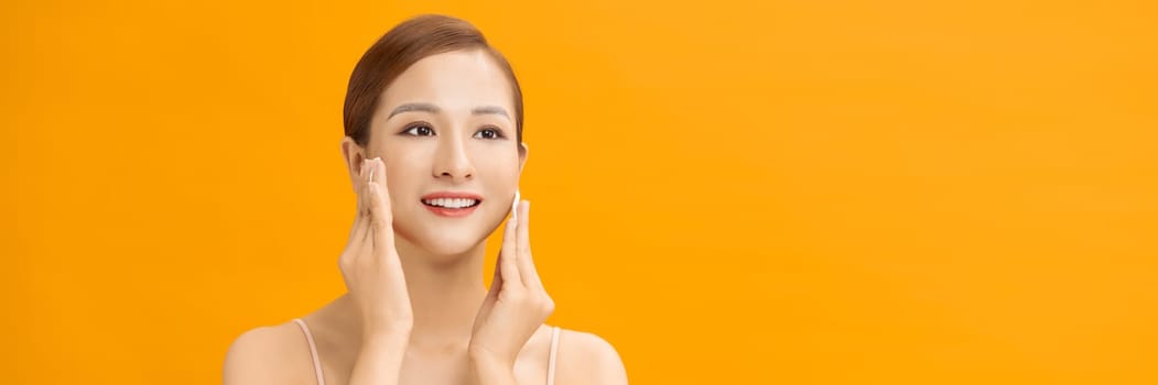 Beautiful young woman cleaning her face with cotton on yellow bachground, banner