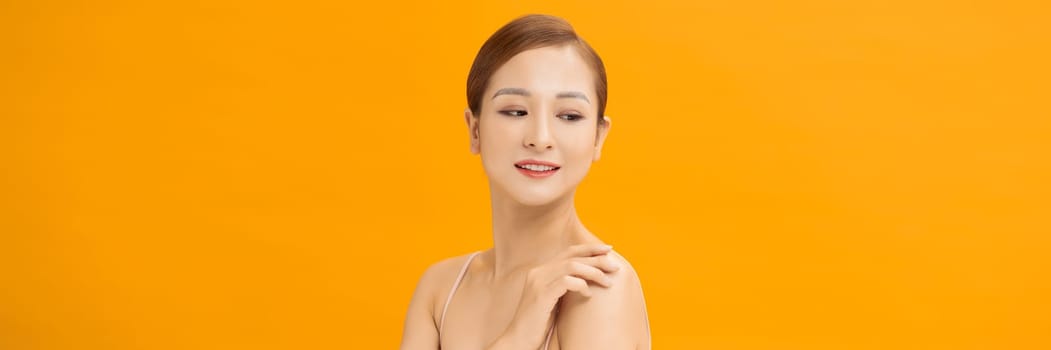 Youthful smiling Asian woman isolated on yellow banner background for beauty and skin care concepts