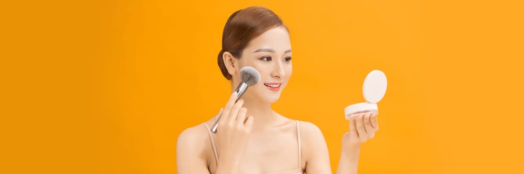 Young woman using brush, applying makeup over banner background