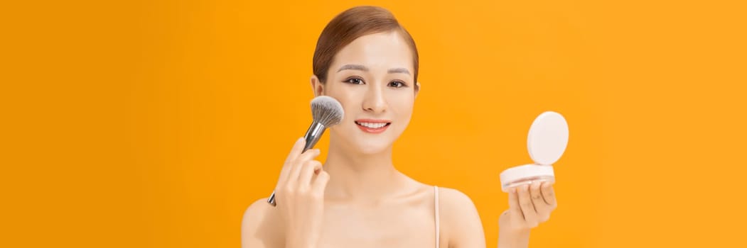 woman applying dry cosmetic tonal foundation on the face using makeup brush on banner background