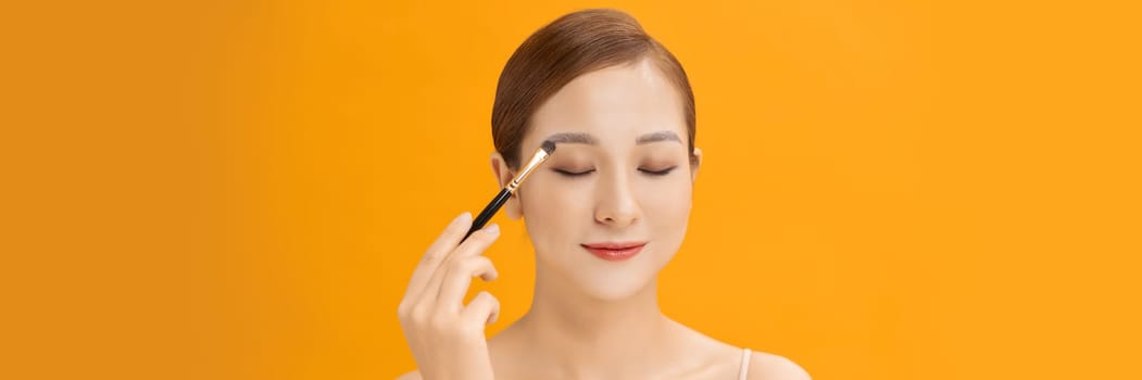 Web banner with young woman with healthy fair skin applying her eyeshadow with brush.