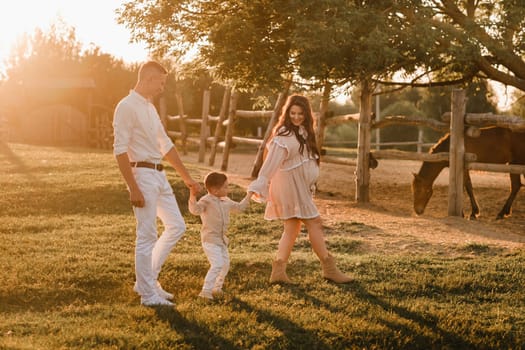 A stylish family in the countryside at sunset. A pregnant woman with her husband and son in nature.