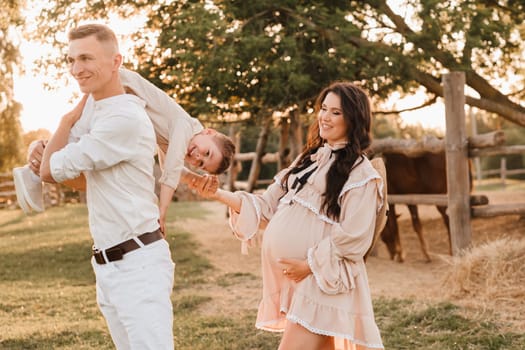 A stylish family in the countryside at sunset. A pregnant woman with her husband and son in nature.