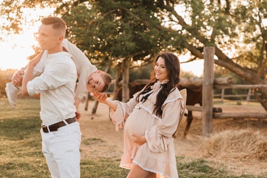 A stylish family in the countryside at sunset. A pregnant woman with her husband and son in nature.