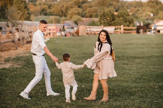 A stylish family in the countryside at sunset. A pregnant woman with her husband and son in nature.