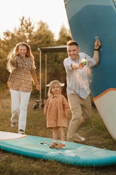 the family is resting next to their mobile home. Dad, mom and daughter play on sup boards with water pistols near the motorhome.