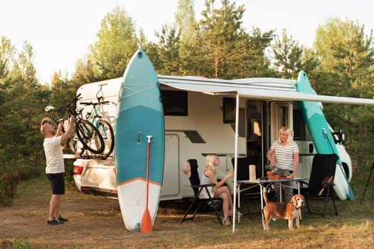 A happy family is resting nearby near their motorhome in the forest.
