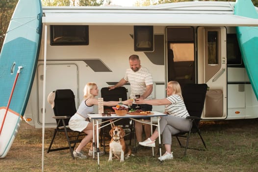 A happy family is resting nearby near their motorhome in the forest.