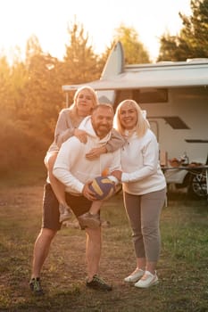 Happy parents with their child playing with a ball near their mobile home in the woods.
