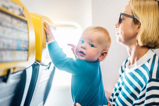 Mom and child flying by plane. Mother holding and playing with her infant baby boy child in her lap during economy comercial flight. Concept photo of air travel with baby. Real people