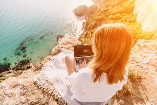 Freelance woman working on a laptop by the sea, typing away on the keyboard while enjoying the beautiful view, highlighting the idea of remote work