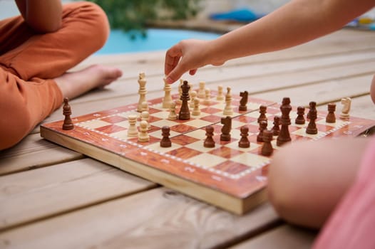 Two children enjoying a game of chess on a wooden deck, showcasing strategy, concentration, and fun during a summer day outdoors.