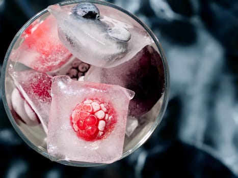 Glass with ice cubes with frozen berries and fruits close-up for a refreshing drink and preservation of seasonal vitamins raspberries, strawberries, cherries, blueberries, mulberries, blackberries