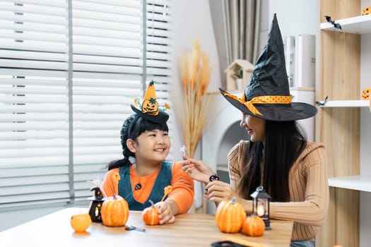 A mother and daughter enjoying Halloween festivities at home, wearing witch hats and surrounded by pumpkin decorations.