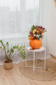 Flower arrangement in a pumpkin, autumn interior decor. Creating handmade autumn decor