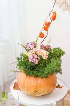 Flower arrangement in a pumpkin, autumn interior decor. Creating handmade autumn decor