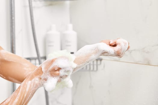 Woman washing her hands with foam bubbles and bath sponge in bathroom. close-up.
