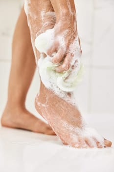 Woman washing her legs with foam bubbles and bath sponge while taking shower in the bathroom