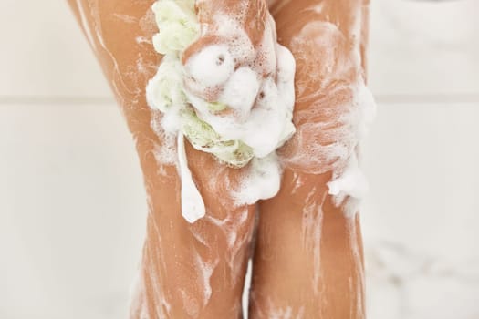 Woman washing her legs with foam bubbles and bath sponge while taking shower in the bathroom