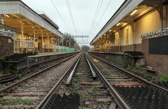 London, UK - Dec 25, 2023 - Perspective view on empty railway tracks and electric infrastructure equipment, wires at Acton central rail station. The Railway system with Metal frames of Train platform, Transport and shipping landscape concept, Railroad track rails, Train tracks, Railway station, Space for text, Selective focus.