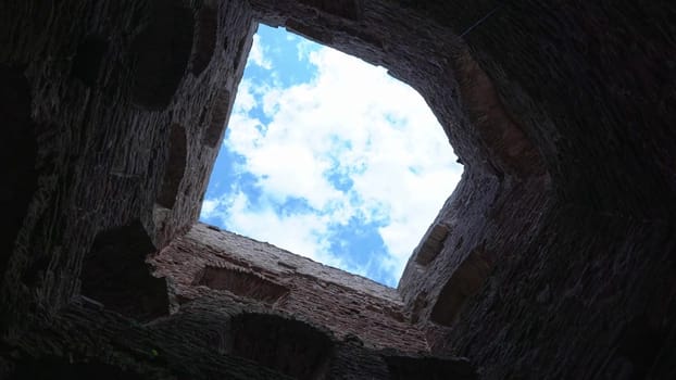 Ancient walls open up to a bright sky filled with clouds.