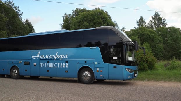 Russia, Pskov region, July 20, 2024 - A A large blue bus rests on a rural road amidst green trees.