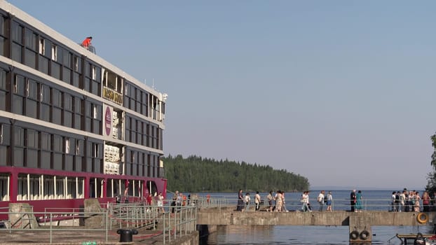 Russia, Valaam Island , July 27, 2024 -Tourists stroll along the dock beside a beautiful lake.