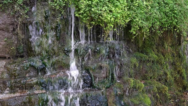 A serene waterfall flows gently down rocky terrain surrounded by greenery.