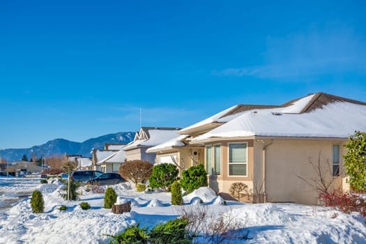 Street of residential houses in snow on winter sunny day. Winter season in suburb in Canada House driveways and front yards in snow