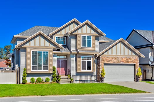 A perfect neighborhood. Suburban family house with concrete driveway and green lawn in front on blue sky background.
