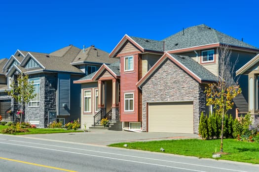 New family house on sunny day with landscaped lawn in front and blue sky background. New house with concrete driveway and asphalt road in front.