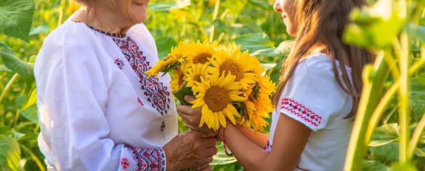 Grandmother and grandchildren in a sunflower field wearing an embroidered shirt. Selective focus. Nature.