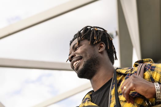 portrait of a smiling young black man passing through a modern metal structure, lifestyle and travel concept