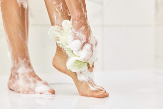 Woman washing her legs with foam bubbles and bath sponge while taking shower in the bathroom
