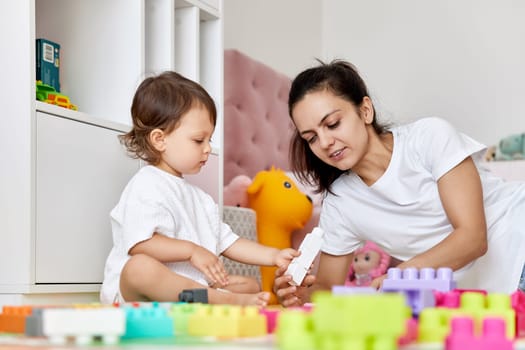 little baby girl and her mother playing with colorful blocks in the children room, having fun together