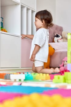 cute baby girl playing with colorful toys bricks in white bedroom