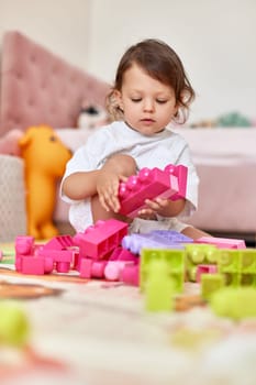 cute baby girl playing with colorful toys bricks at home
