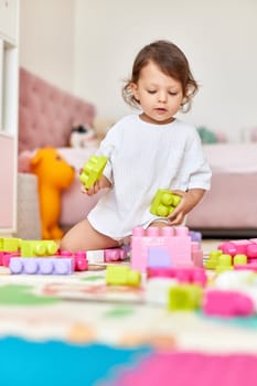 cute baby girl playing with colorful toys bricks at home