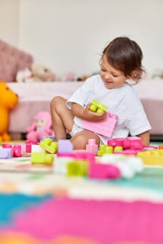 cute baby girl playing with colorful toy blocks in her room