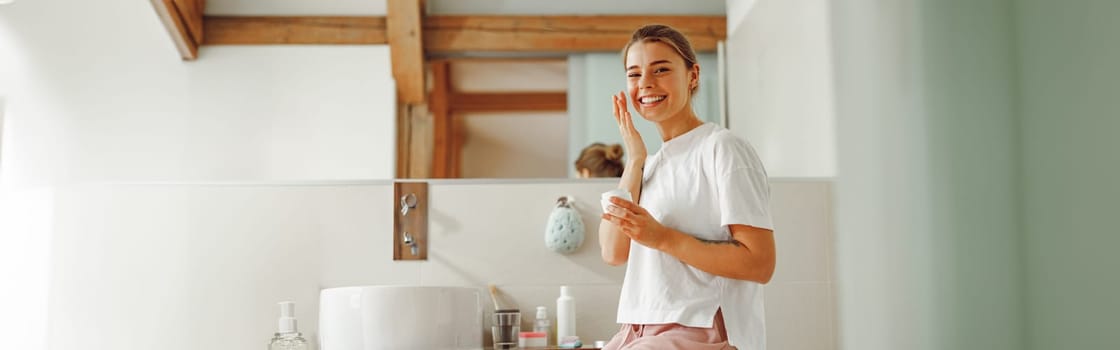 Young woman holding jar with skincare cream in hands. Home beauty routine