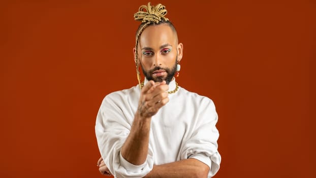African american gay man in white clothes points index finger at camera isolated on red background, handsome multiracial guy choosing you studio portrait Make up and fashion lgbtq concept