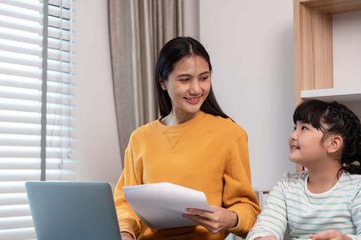 A mother and daughter share a joyful moment at home, working on a laptop and holding documents, showcasing family bonding and togetherness.
