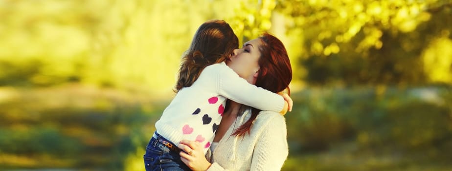 Family bonding moment, happy young mother kissing her child, little daughter hugs mom in sunny park