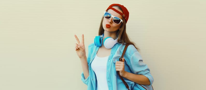 Stylish modern young woman listening to music with headphones, cool girl in baseball cap posing on white background